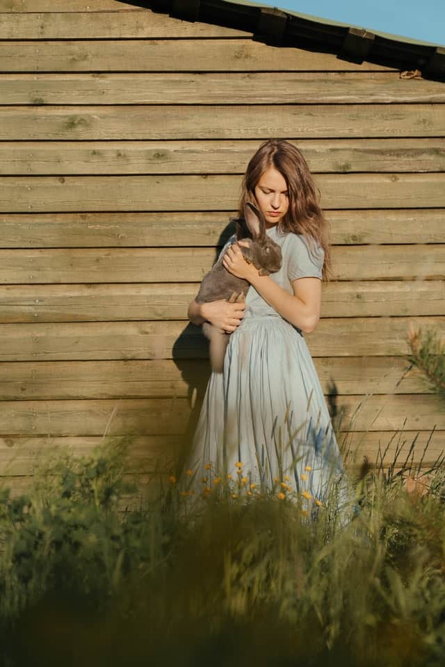 A person sitting quietly on the floor near a rabbit offering a treat